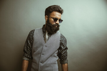 Obraz premium Bearded young businessman posing with sunglasses on gray.
