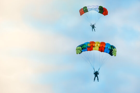 two skydivers on brightly colored parachutes soar above each other high in the blue sky