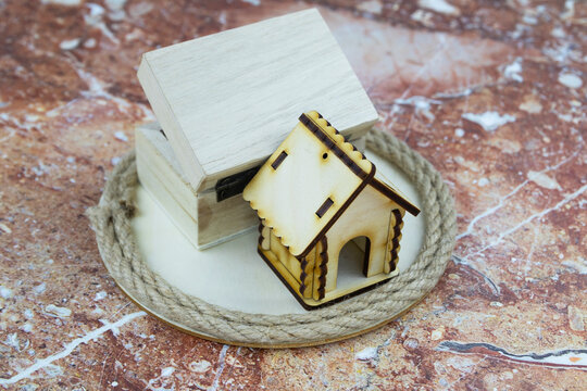 Conceptual financial still life with model house next to small wooden box with spiral rope for home ownership. High quality photo