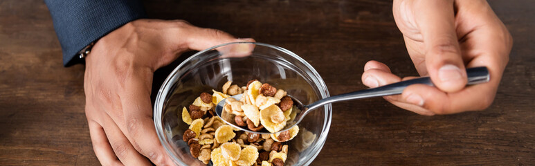 partial view of african american man holding spoon near corn flakes in bowl, banner.