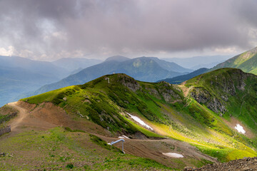 Landscape of green valley, forested mountains and a bit of snow on a grass