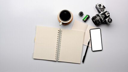 Top view of workspace with blank notebook, smartphone, camera and coffee cup