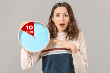 Woman holding clock with timer for 10 minutes on grey background. Time management concept