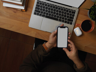 Male hand using smartphone on worktable with laptop and supplies