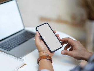 Male hands using smartphone while working with laptop on coffee table