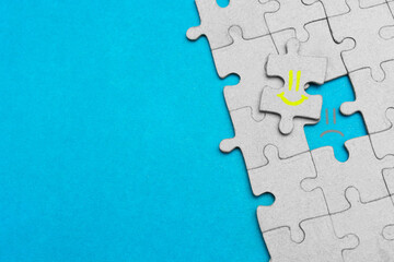 Fake emotions, play role concept. False joy, fake happiness. Jigsaw mosaic puzzle with yellow happy smiley face and sad smiley face on light blue background with copy space. Happiness and sadness