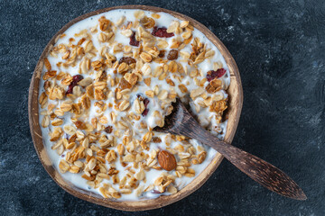 Granola with oatmeal, dried fruit, honey, raisins, dry cranberry, almond and cashew nuts with yogurt in a coconut bowl, close up
