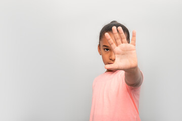 Studio shot of young  dark skinned girl gesturing to stop with her hand out against grey background