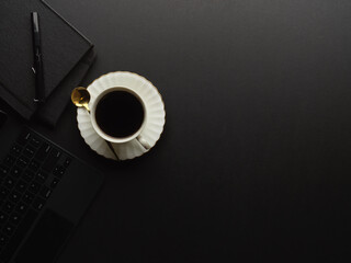 Top view of black table with coffee cup, stationery, laptop and copy space