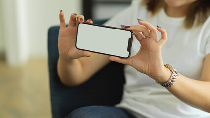 Female hands showing horizontal smartphone while sitting on arm chair