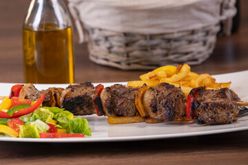 roasted beef skewer with freshly cut vegetables and french fries on a plate