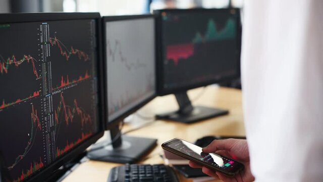 Man showing information on smartphone. Male and female stockbrokers in formal clothes works in the office with financial market and graphs on monitors.