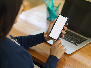 Cropped shot of businesswoman using smartphone while working with laptop
