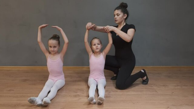 Two young students on ballet class. The professional ballerina is stretching with two little girls.