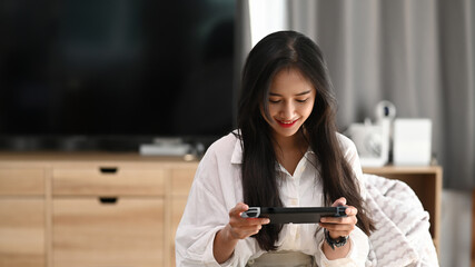 A young female in pajamas playing video games and sitting on sofa at home.