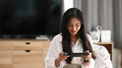 A young female in pajamas playing video games and sitting on sofa at home. © Prathankarnpap