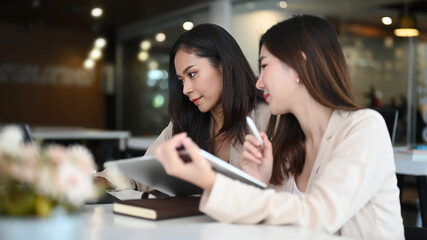 Two successful businesswomen discussing company financial strategy and planning profitability  while sitting at desk in office.