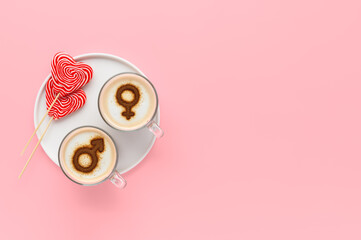 Two cups of coffee with symbols of venus and mars on whipped milk foam and couple of lollipops in heart shape. Pastel pink background. Concept romantic breakfast on Valentine's day. copy space © Ramil Gibadullin
