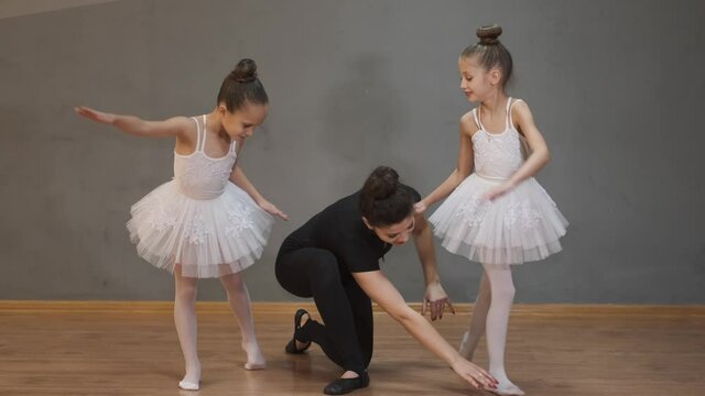 Two young students on ballet class. The professional ballerina is stretching with two little girls.