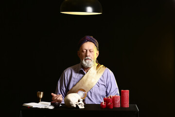 Male fortune teller at table on dark background