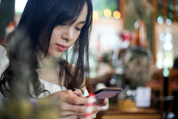 Beautiful Asia woman use smart phone in coffee shop with Bokeh background Soft focus.