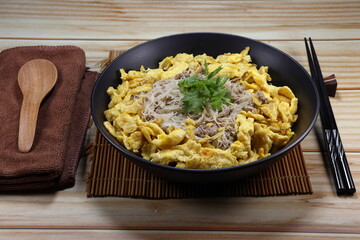 Stirred rice noodle topping with fried chicken egg (Scramble egg) serving on the plate. Famous breakfast menu in Asia restaurant. 