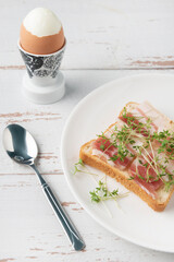 Plate with slices of bacon and watercress microgreens on white wooden table