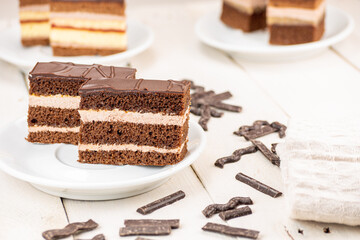 Chocolate cake with three chocolate  dough and two cream floors. Ideal wedding and celebration dessert. Served on white wooden retro table with two another kinds of desserts. 