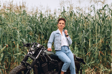 Proud, confident and adult girl wearing denim casual clothes and sitting and posing on a black retro motorcycle. Green background. Retro concept