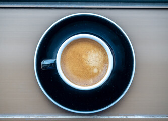 Top view for coffee in black ceramic cup with round dish beneath on table, for background