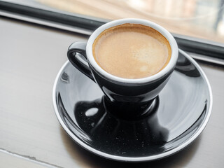 Coffee in ceramic black cup and round dish beneath at window light view, for background