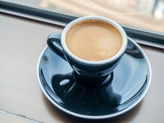 Coffee in ceramic black cup and round dish beneath at window light view, for background