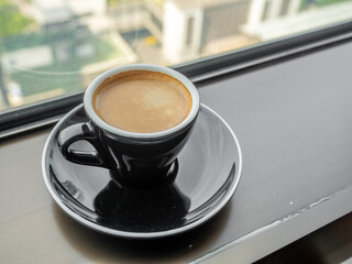 Coffee in ceramic black cup and round dish beneath at window light view, for background