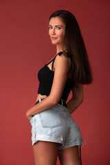 beautiful woman in a black top and denim shorts posing in the studio on a red background