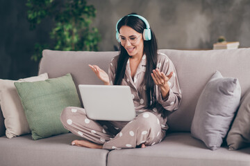 Photo of nice optimistic girl sit talk laptop wear spectacles headphones pijama at home