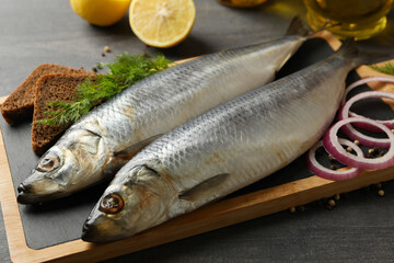 Board with herring fish and spices, and oil on dark wooden background