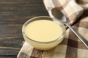 Towel, spoon and bowl with condensed milk on wooden background
