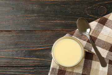 Towel, spoon and bowl with condensed milk on wooden background