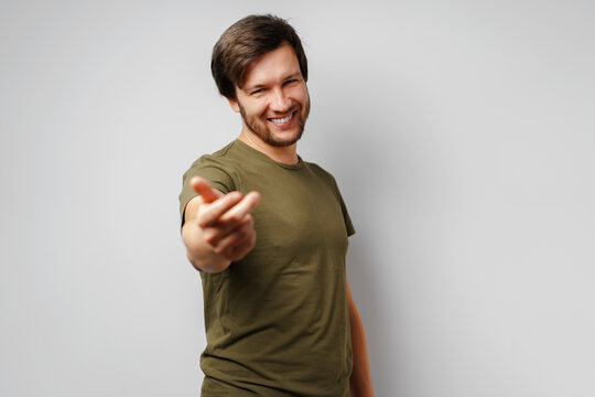 Young man in green t-shirt smiling and gesturing 'come here'