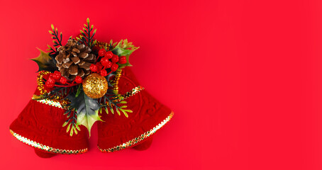 Red bells with pine cones, twigs of trees, berries and gold decorations on a red background. Banner. Concept of a Christmas greeting card. Space for text.