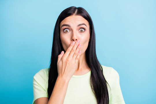 Photo portrait of shocked girl closing mouth with one hand isolated on pastel blue colored background