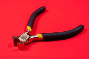 The construction tool ticks pliers metal steel with a black handle on an red background. For...