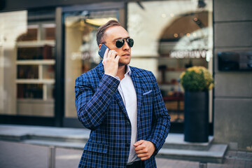 young stylish man holding a mobile phone in the city center. Man wearing jacket and shirt
