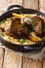 Yemeni dish of baked lamb shank served with aromatic rice close-up in a frying pan on the table. vertical