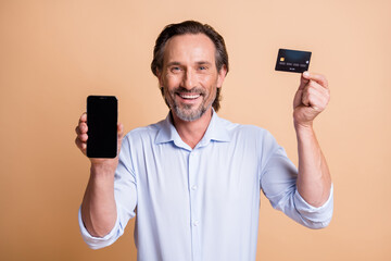 Photo of man demonstrate telephone screen empty space hold credit card wear shirt isolated beige color background