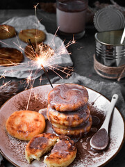 Sweet cottage cheese pancakes. Condensed milk. Festive sweet breakfast or lunch. Dark Grey background. Food and sparklers.