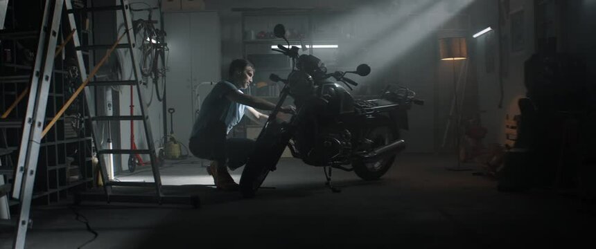 Caucasian male performing maintenance of his vintage motorcycle at home garage. Shot with 2x anamorhpic lens