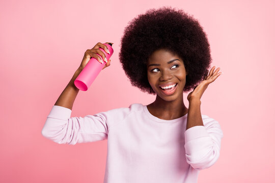 Portrait of pretty cheerful wavy-haired girl applying spray on hair modern care fixing isolated over pink pastel color background