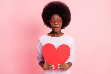 Portrait of pretty cheerful amazed wavy-haired girl holding in hands heart shape romance pout lips isolated over pink color background