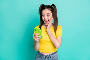 Photo of impressed cute woman dressed yellow t-shirt holding looking modern gadget arm cheek isolated teal color background